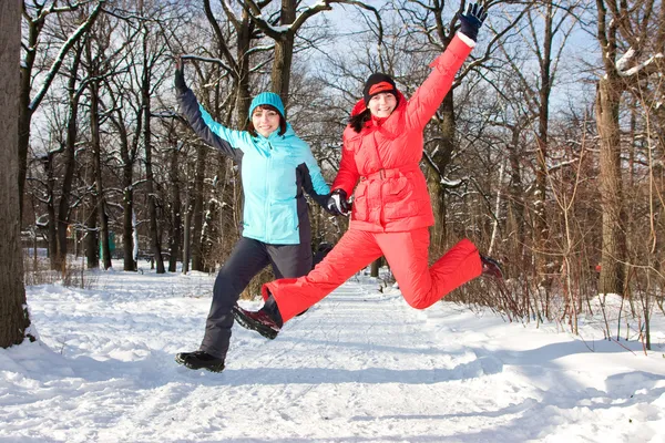 Two cheerful friendly girls jump in park