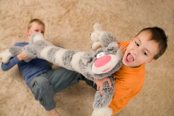 Two kids with a toy cat on the floor
