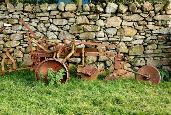 Old rusty plow in shadow of stone wall