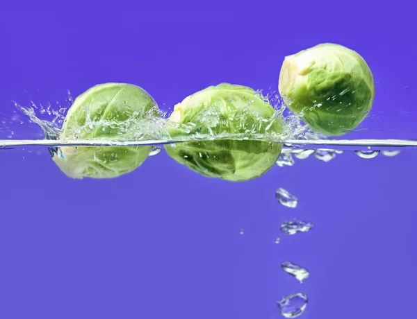 Three Brussels sprouts falling in water