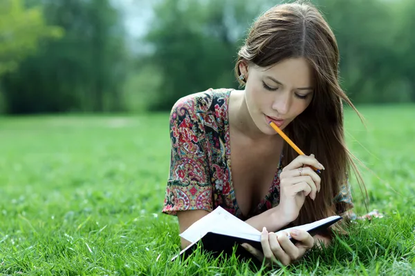 Woman lays on a grass in park with a diary in hands