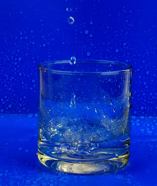Glass of water and drops on a dark backg