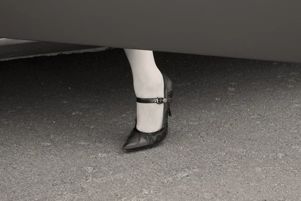 Female leg in a high heel shoe at a car