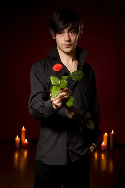 Young man with rose in black shirt on red backg