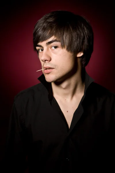 Young man with toothpick in black shirt on red