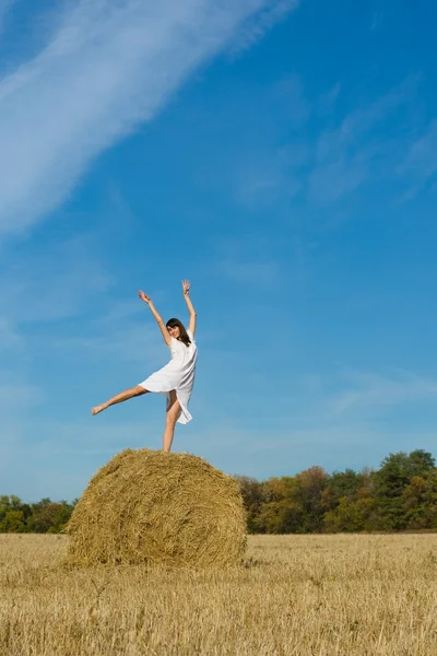 Pretty girl dance on haystack in field