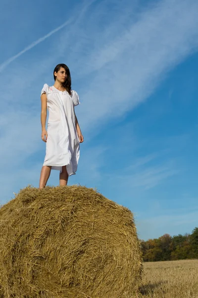 Girl in white dress on haystack in field