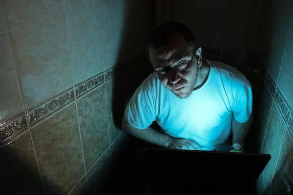 Man with laptop sitting in a dark room