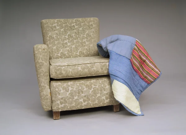 An old worn out armchair with quilt style blanket, studio shoot, grey background