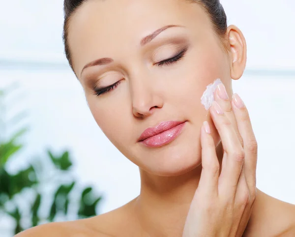 Woman applying cream on cheek