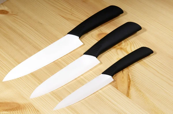 Set of white ceramic knives on woodboard