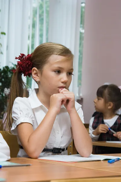 The sad girl sits at a school desk
