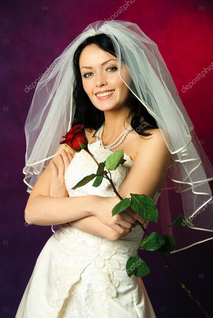 Sexy brunette bride wearing a white wedding dress and a veil with a red rose