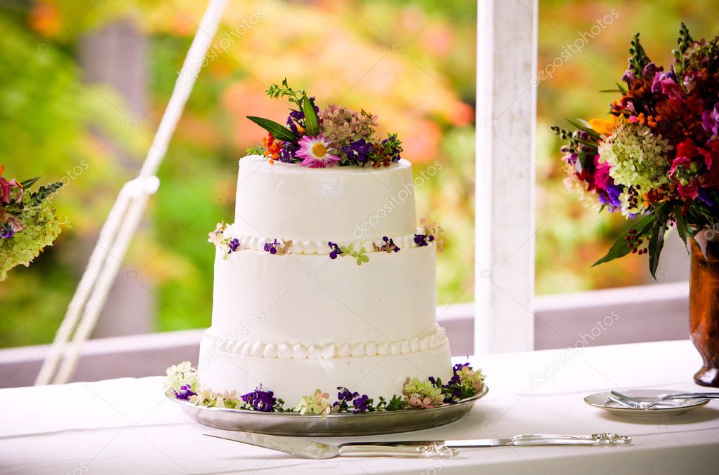  wedding cake with flowers outside in front of a colorful autumn backdrop