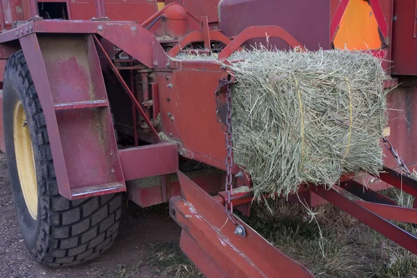 Square bale of hay coming out of farm machinery