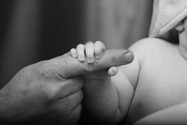 A baby holds her father\'s finger
