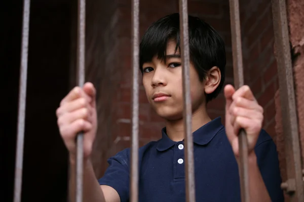 Boy standing behind bars
