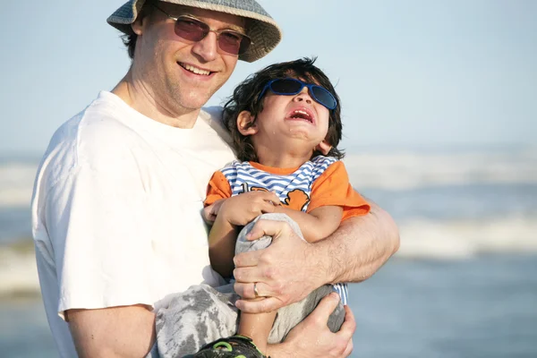 Father holding crying child at beach