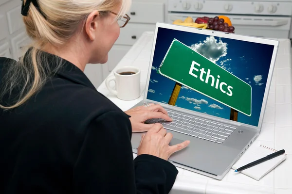 Woman In Kitchen Using Laptop with Ethics Road Sign on Screen