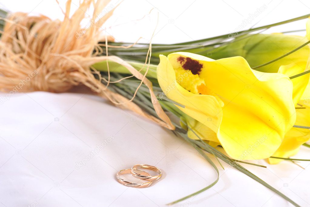 yellow calla lilies and wedding rings isolated on white silk