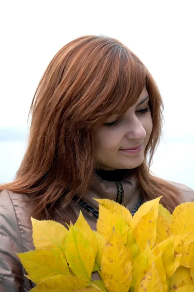 年轻的红发女孩用黄色叶子 图库图片