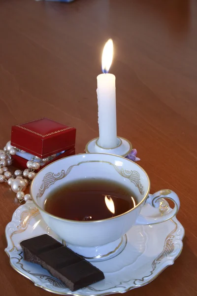 Boné de porcelana fina de chá, Chocolate e vela em chamas na mesa — Fotografia de Stock