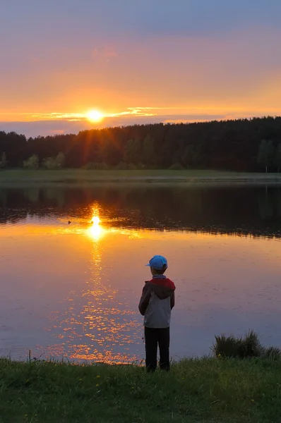 Хлопчик на березі озера на заході сонця — стокове фото