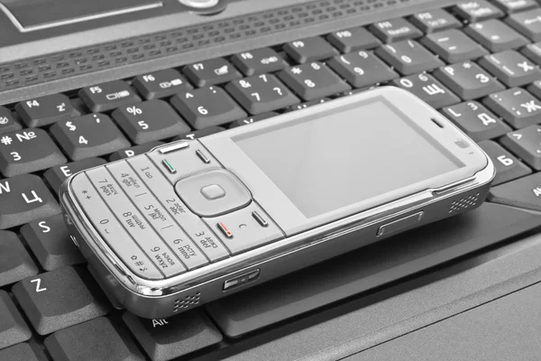 Teléfono móvil se encuentra en el teclado del ordenador portátil —  Fotos de Stock