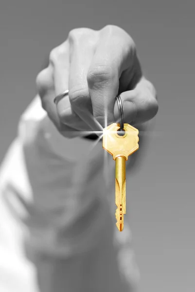 Hand houdt een gouden sleutel (in focus) — Stockfoto