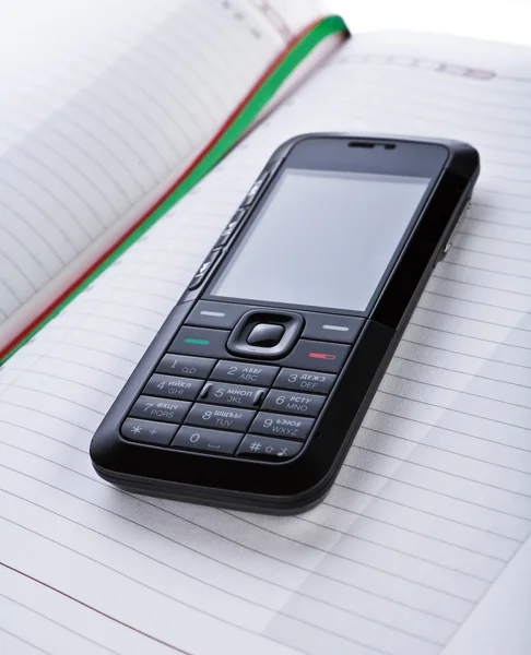 Telefone celular preto em um bloco de notas — Fotografia de Stock