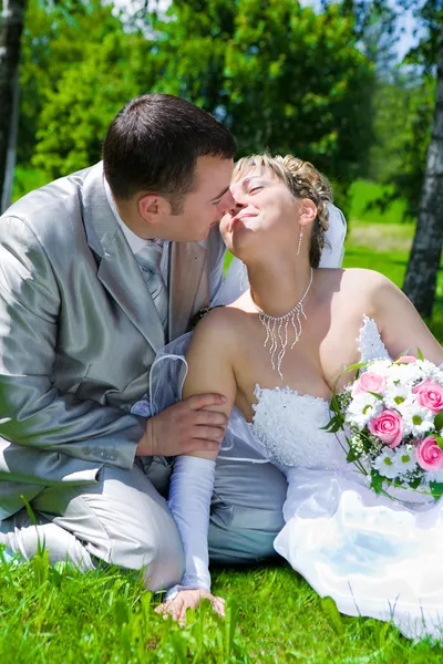 Svatební pár sedí na trávě kiss — Stock fotografie