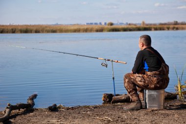 Sitting fisherman with a fishing tackle clipart