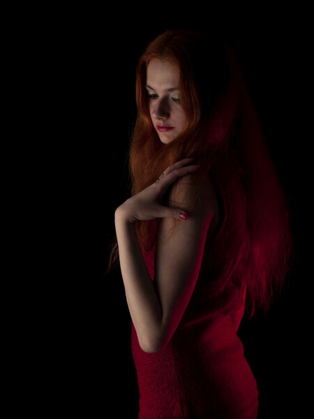 Beautiful red-haired young lady in evening dress on black background