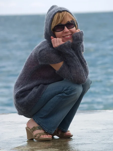 Youn signora in cappuccio seduta vicino al mare — Foto Stock