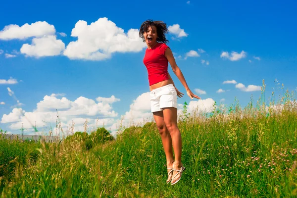 Lycklig ung kvinna hoppar i ett fält — Stockfoto