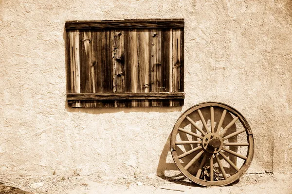 Παλιά ξύλινη πινακίδα και τροχό δίπλα σε τοίχο — Φωτογραφία Αρχείου