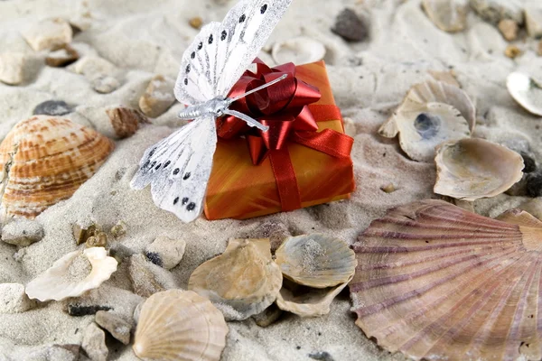 Gift and butterfly in the sand — Stock Photo, Image