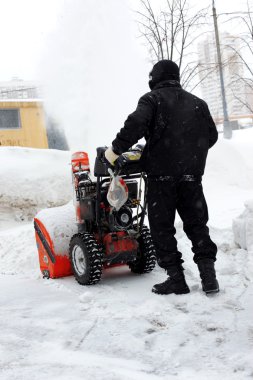 Snowblower in city under snowfall clipart