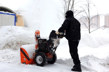 Snowblower in city under snowfall clipart