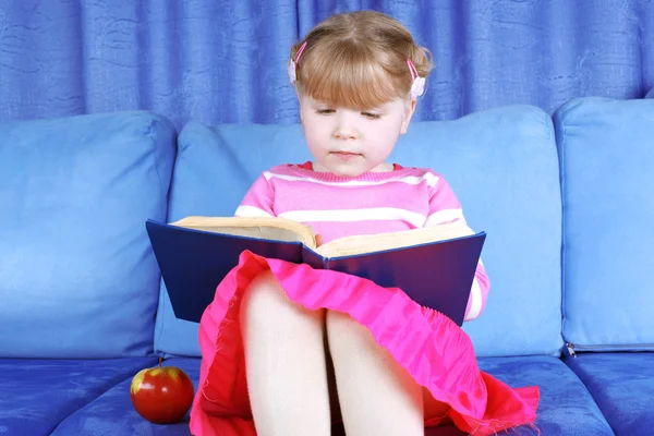 Mädchen liest Buch mit Apfel auf Sofa — Stockfoto