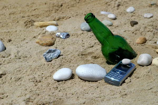 Bottle with cellular phone on sand — Stock Photo, Image