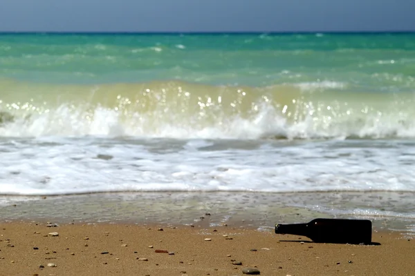 Бутылка на песке возле воды — стоковое фото