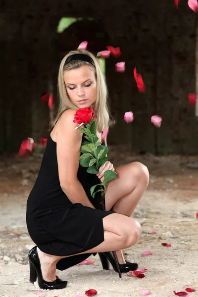 Vrouw met roos onder vallende bloemblaadjes — Stockfoto