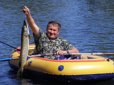 The fisherman in the boat with a pike clipart