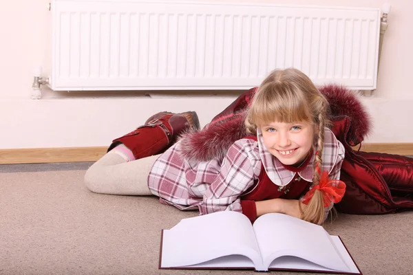 Menina mentira perto radiador com livro . — Fotografia de Stock
