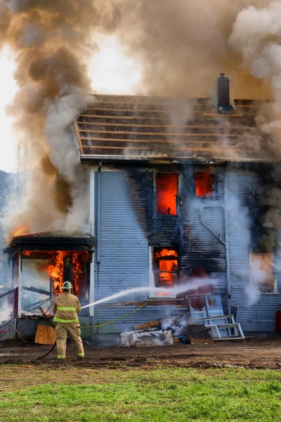 Pompier arrosant une maison en feu — Photo