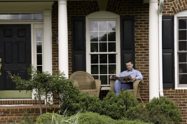 Man reading newspaper on porch clipart