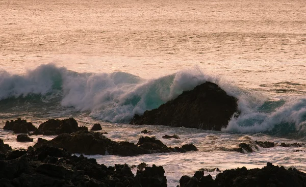 Разбивая волны на скале на закате — стоковое фото