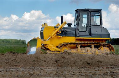 Bulldozer in fields over blue cloudy sky clipart