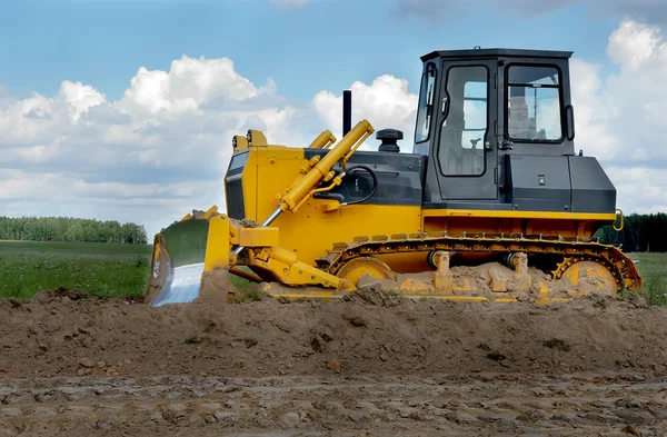 Bulldozer in fields over blue cloudy sky — Stock Photo, Image